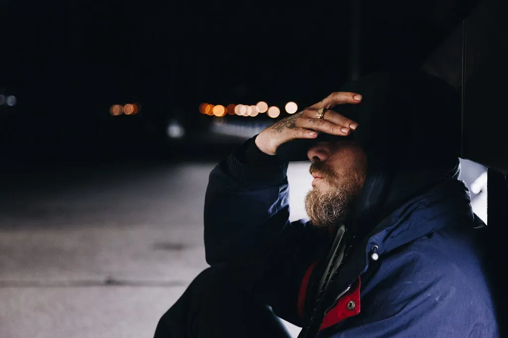 A man in a hooded jacket at night, one hand over his eyes